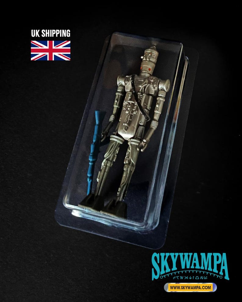 May include: A silver-colored droid action figure with a slender, mechanical frame and a cylindrical head, encased in a clear plastic blister pack. The figure holds a long, blue rifle-like accessory in its right hand and features intricate molded details.