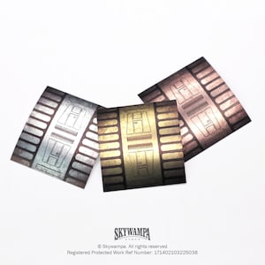 Pode incluir: Três folhas de metal com um padrão geométrico em prata, ouro e cobre.