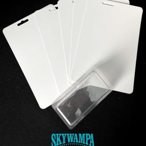Può includere: Un set di cinque cartoncini espositivi rettangolari bianchi e vuoti con angoli arrotondati e un foro centrale nella parte superiore, disposti a ventaglio. Un blister in plastica trasparente è fissato sul davanti. Il testo SKYWAMPA e WWW.SKYWAMPA.COM appare in basso.