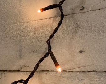 May include: A string of warm white fairy lights with brown wire, strung across a white wooden wall.