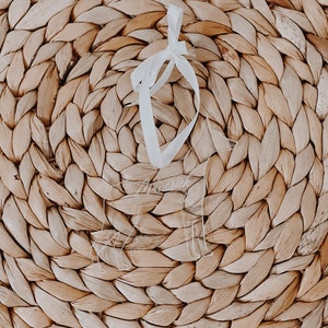 May include: A clear acrylic ornament in the shape of a dog, with the name "Maverick" etched on it. The ornament hangs from a white ribbon against a woven, light brown background.