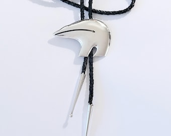 May include: A silver bolo tie featuring a polar bear pendant with a black braided cord. The bear has a sleek, minimalist design. The cord ends with silver tips.