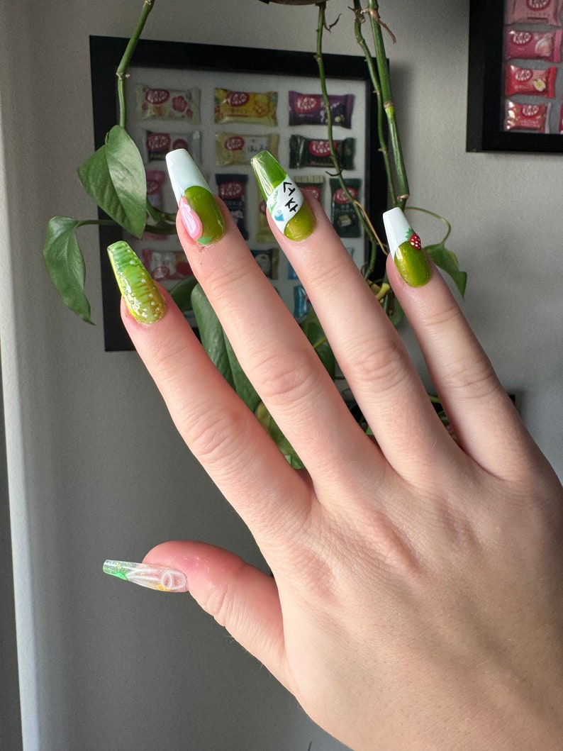 May include: Green and white long, almond-shaped fake nails with a floral design and the text "LYH" on one nail.