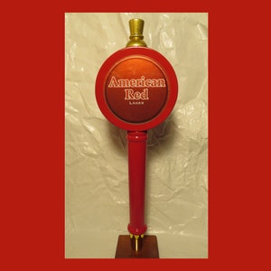 May include: Red and gold beer tap handle with the words "American Red Lager" on the front.