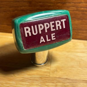 May include: Green and red beer tap handle with the words "Ruppert Ale" on it.