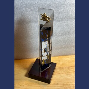 May include: A Budweiser ICE tap handle with a gold-colored emblem and the Budweiser logo. The tap handle is clear with a black, blue, and white design. It is mounted on a dark brown wooden base.