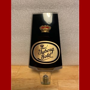 May include: A black and gold beer tap handle with a gold crown and the text "Tuborg Gold".