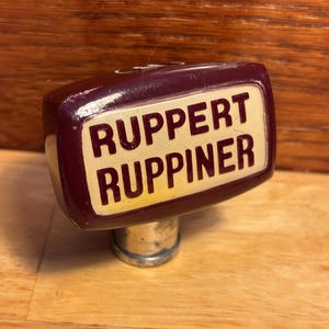 May include: A burgundy-colored beer tap handle with a white label that reads "Ruppert Ruppiner".