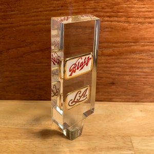 May include: A clear acrylic beer tap handle with gold trim and red and white labels that say "Blatz" and "L.A."
