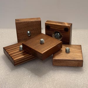 May include: Five square wooden blocks with a rich brown stain. Each block has a metal bolt protruding from the top or side. The blocks are arranged in a slightly overlapping pattern, showcasing their varying textures and finishes.