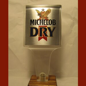 May include: A silver and clear plastic beer tap handle with a gold eagle and the text "Michelob Dry" in blue and red.