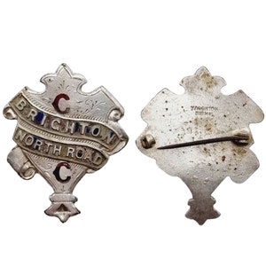 Könnte beinhalten: Silberfarbener Anstecker mit einem Design aus blauem, rotem und goldenem Emaille. Der Anstecker trägt den Text "Brighton North Road C" und eine Herstellermarke auf der Rückseite, die "Yaugton Birmingham" lautet.