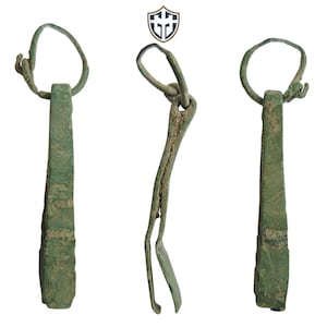 Puede incluir: Tres vistas de una herramienta antigua de bronce. La herramienta tiene un mango rectangular con un lazo en la parte superior y un extremo bifurcado. El bronce tiene una pátina verde, lo que indica la edad. La herramienta es probablemente un artefacto histórico.
