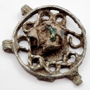 May include: A circular silver-colored pendant with an intricate openwork design. The pendant features a central green glass stone.