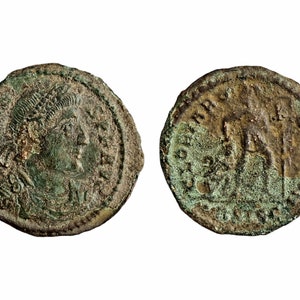 Puede incluir: Una moneda romana de bronce con el retrato de un emperador romano en una cara y una figura de pie en la otra.