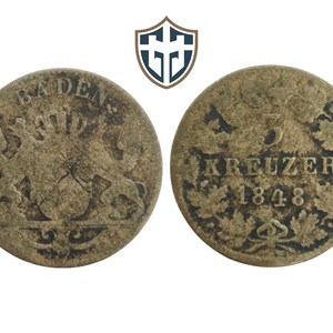 Puede incluir: Dos monedas antiguas, una con la palabra "BADEN" y un escudo, la otra con "5 KREUZER 1848" rodeada de hojas. Las monedas son de color bronce desgastado, con signos visibles de desgaste.