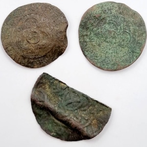 Puede incluir: Tres monedas antiguas de cobre con escritura árabe. Las monedas están desgastadas y tienen una pátina verde. Una moneda está completa, mientras que las otras dos están rotas.