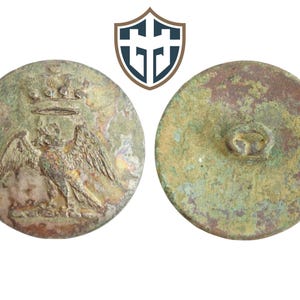 May include: A vintage metal button featuring a raised design of a crowned eagle. The reverse of the button is plain and shows signs of wear.