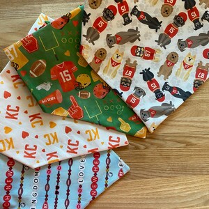 K&ouml;nnte beinhalten: Eine Auswahl an Hunde-Bandanas mit verschiedenen Mustern. Eines zeigt Football-Grafiken mit der Nummer 15, ein anderes zeigt Hunde-Illustrationen in Football-Trikots mit den Nummern 15 und 87. Andere Bandanas haben den Text "KC", "REACH NEW" und "LOVE".