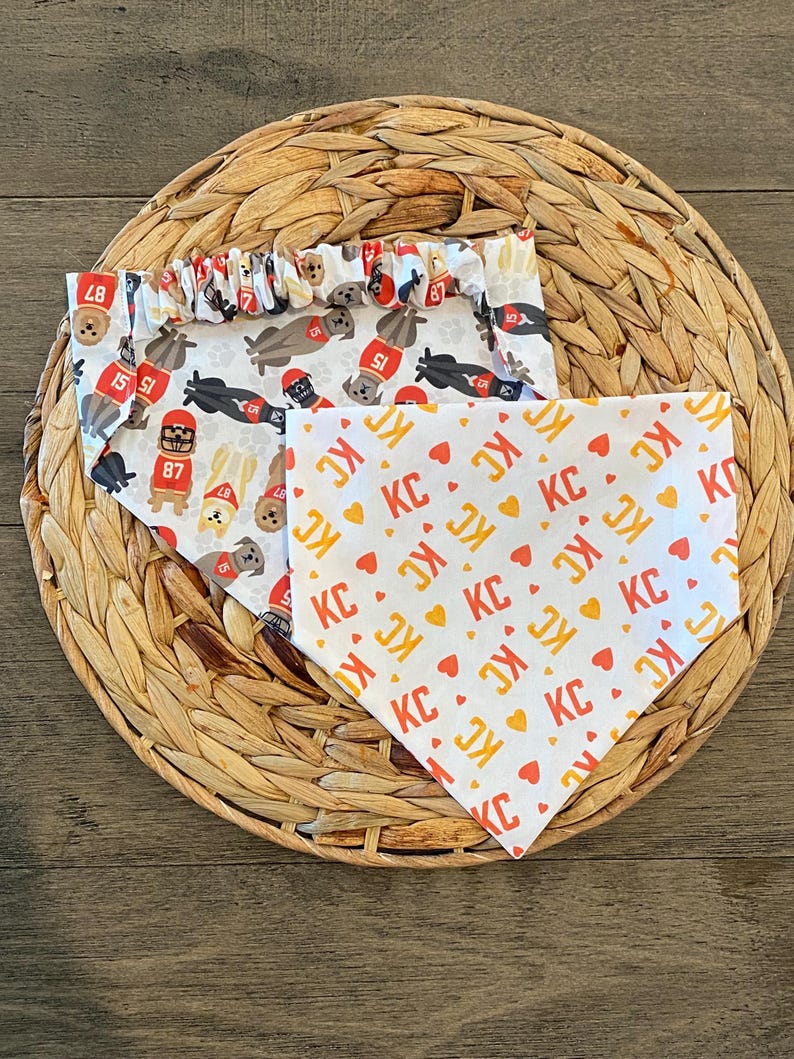 K&ouml;nnte beinhalten: Zwei Hunde-Bandanas auf einer gewebten Matte. Ein Bandana hat einen wei&szlig;en Hintergrund mit sich wiederholenden Bildern von Hunden mit Football-Helmen und den Zahlen 15, 51 und 87. Das andere Bandana hat einen wei&szlig;en Hintergrund mit sich wiederholenden "KC"- und Herzmustern.