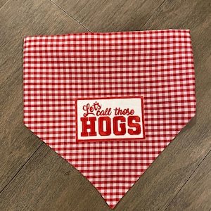 May include: Red and white gingham dog bandana with the text "Let's call those HOGS" in red lettering. The bandana is a triangle shape, perfect for pets.