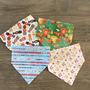 K&ouml;nnte beinhalten: Vier Hunde-Bandanas mit verschiedenen Mustern. Eines zeigt Football-Motive mit den Nummern 15 und 87. Ein anderes hat ein sich wiederholendes "KC"-Muster. Das dritte hat den Text "LOVERS IN KC" und "REACH NEW HEIGHTS". Das letzte hat Hunde und Fu&szlig;b&auml;lle.