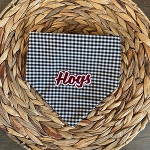 May include: A triangular pet bandana featuring a black and white gingham check pattern. The word Hogs is printed in the center in a bold, stylized white font with a thick maroon outline, creating a clear contrast against the checkered fabric.