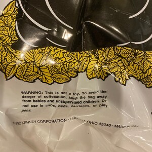 May include: A white plastic bag with a black graphic design and yellow leaf accents. The bag has a warning label with text about suffocation hazards and the text "&copy;1992 KENLEY CORPORATION - MA OHIO 45040 - MADE IN USA."