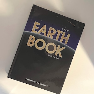 May include: A hardcover "EARTH BOOK" world atlas with a dark blue cover featuring gold lettering. The book's title is prominently displayed, with the words "CONCISE" and "WORLD ATLAS" also visible. The publisher's name, "EARTHBOOKS INCORPORATED," is printed at the bottom.