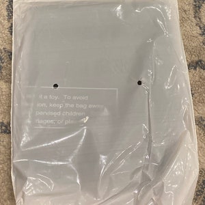 May include: A sealed, clear plastic bag with a white top. The bag contains an item that is not visible. Text on the bag reads: "...it a toy. To avoid...pervised children..."
