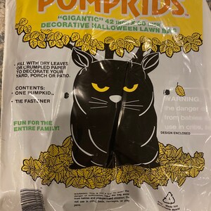 May include: A clear plastic bag containing a black cat-shaped lawn decoration for Halloween. The bag has yellow and orange text that reads "PUMPKIDS" and "GIGANTIC 42 IN x 60 INCH DECORATIVE HALLOWEEN LAWN BAG". The cat has yellow eyes.