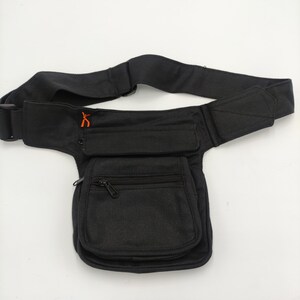 Pode incluir: Bolsa de cintura preta de lona com um bolso com zíper e um bolso grande com aba. A bolsa tem um cinto largo ajustável.