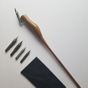 May include: A wooden calligraphy pen with a long, slender handle and a metal nib. Five additional nibs are included, along with a black leather pouch.