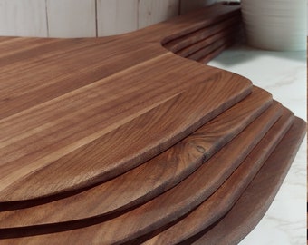 May include: A set of five wooden pizza peels, stacked on top of each other. The peels are made of dark brown wood and have a rounded, slightly curved shape. The peels are sitting on a white marble surface.