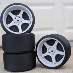 May include: Four black and white wheels stacked on top of each other. The wheels have a five-spoke design and a white rim.