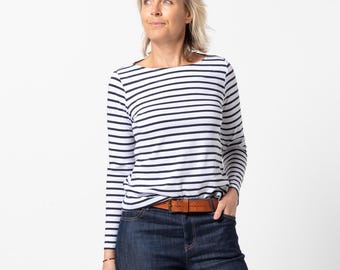 May include: A long-sleeved shirt with a white and navy blue horizontal striped pattern, paired with dark blue denim jeans, a brown leather belt with a metal buckle, and tan woven leather sandals. The outfit features a classic boat neckline.