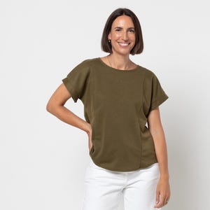 May include: An olive green top with short sleeves and white wide-leg trousers. The top has a round neck and a seam detail down the front. The trousers are white. The person is wearing sandals.