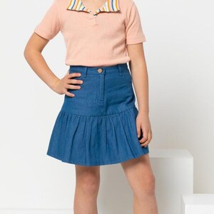 May include: A young person wearing a peach-colored polo shirt with a striped collar and a blue denim skirt. The outfit is completed with white high-top sneakers. The background is white.