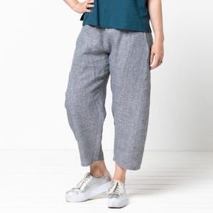 May include: A woman is wearing a teal blue short-sleeved top and gray cropped pants. She is wearing silver sneakers.