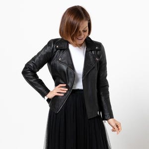 Peut inclure: Veste en cuir noir avec fermeture éclair asymétrique et col à revers. La veste est portée avec un haut blanc et une jupe en tulle noire. L'ensemble est posé sur un fond blanc. Style motard classique.
