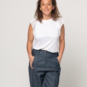 May include: A woman wearing a white sleeveless top with eyelet detailing on the sleeves and dark blue denim pants.