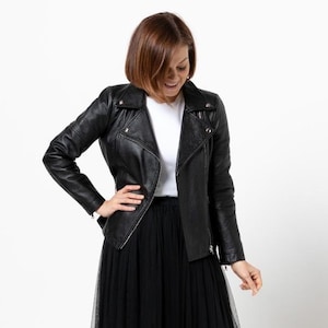 May include: A black leather jacket with a classic asymmetrical zipper design. The jacket has a notched collar and long sleeves. The model is wearing a white shirt and a black tulle skirt.