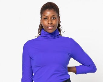 May include: A woman wearing a long-sleeved, bright blue turtleneck shirt with a high collar. She is wearing blue jeans and has her hair pulled back.