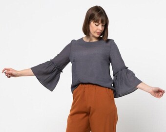May include: A gray, long-sleeved blouse with ruffled sleeves and a round neckline. The blouse is paired with rust-colored pants.