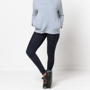 May include: A woman is wearing a light blue sweater and black leggings. She is wearing black sneakers with green accents.