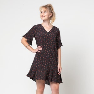 Op de afbeelding: Een zwarte jurk met rode bloemenprint, een v-hals en korte mouwen. De jurk heeft een gerimpelde zoom en wordt gedragen met zwarte wedges.