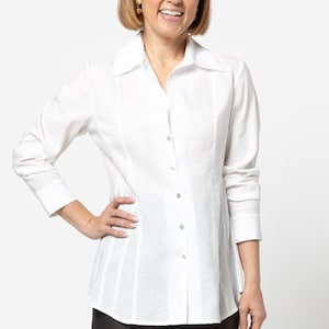 May include: A white long-sleeved button-down shirt with a collared neckline. The shirt has a fitted silhouette and a slightly longer length.