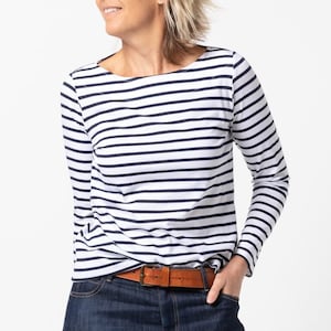 May include: A white and navy blue striped long-sleeve shirt with a boat neck. The shirt is worn with a brown leather belt and blue jeans.