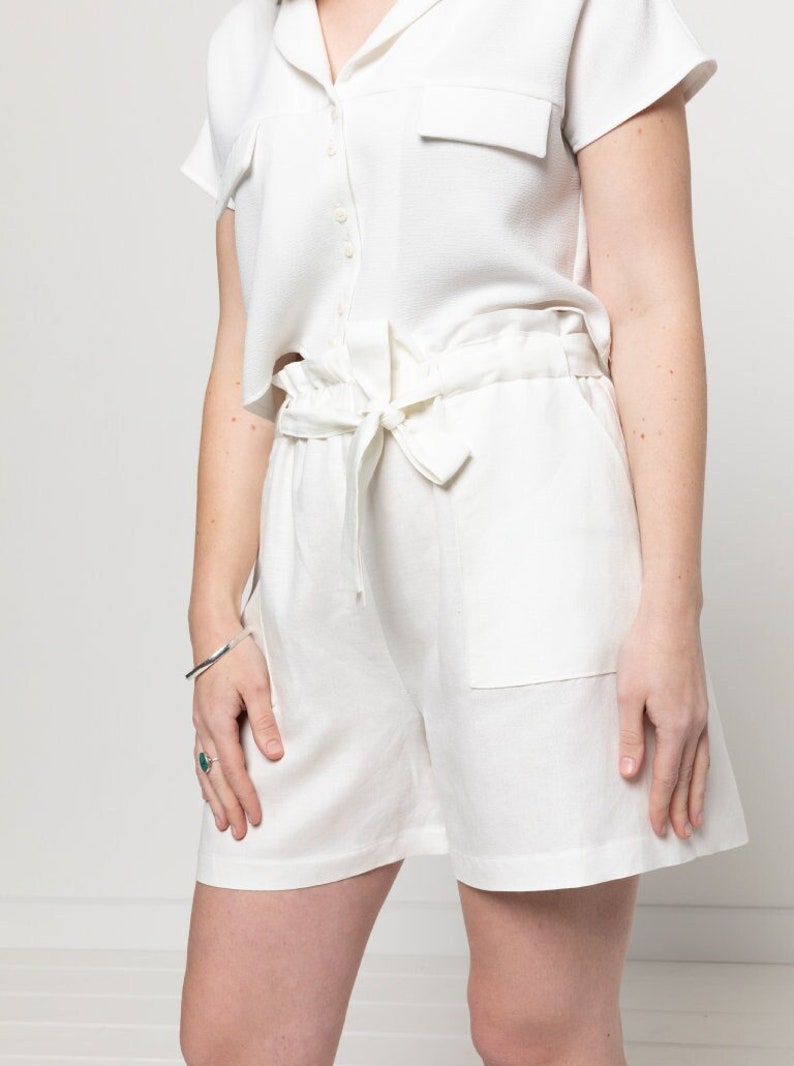 May include: White linen shorts with a tie waist and a patch pocket on the right side.