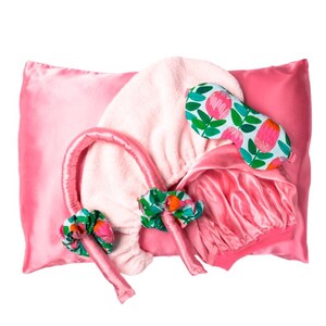 Könnte beinhalten: Ein pinkfarbenes Satin-Schlafset mit Kissenbezug, Schlafmaske, Haarwickel und Lockenwicklern. Die Schlafmaske und Lockenwickler weisen ein Blumenmuster mit rosa, grünen und orangefarbenen Akzenten auf. Das Set ist für Komfort und Schönheit konzipiert.